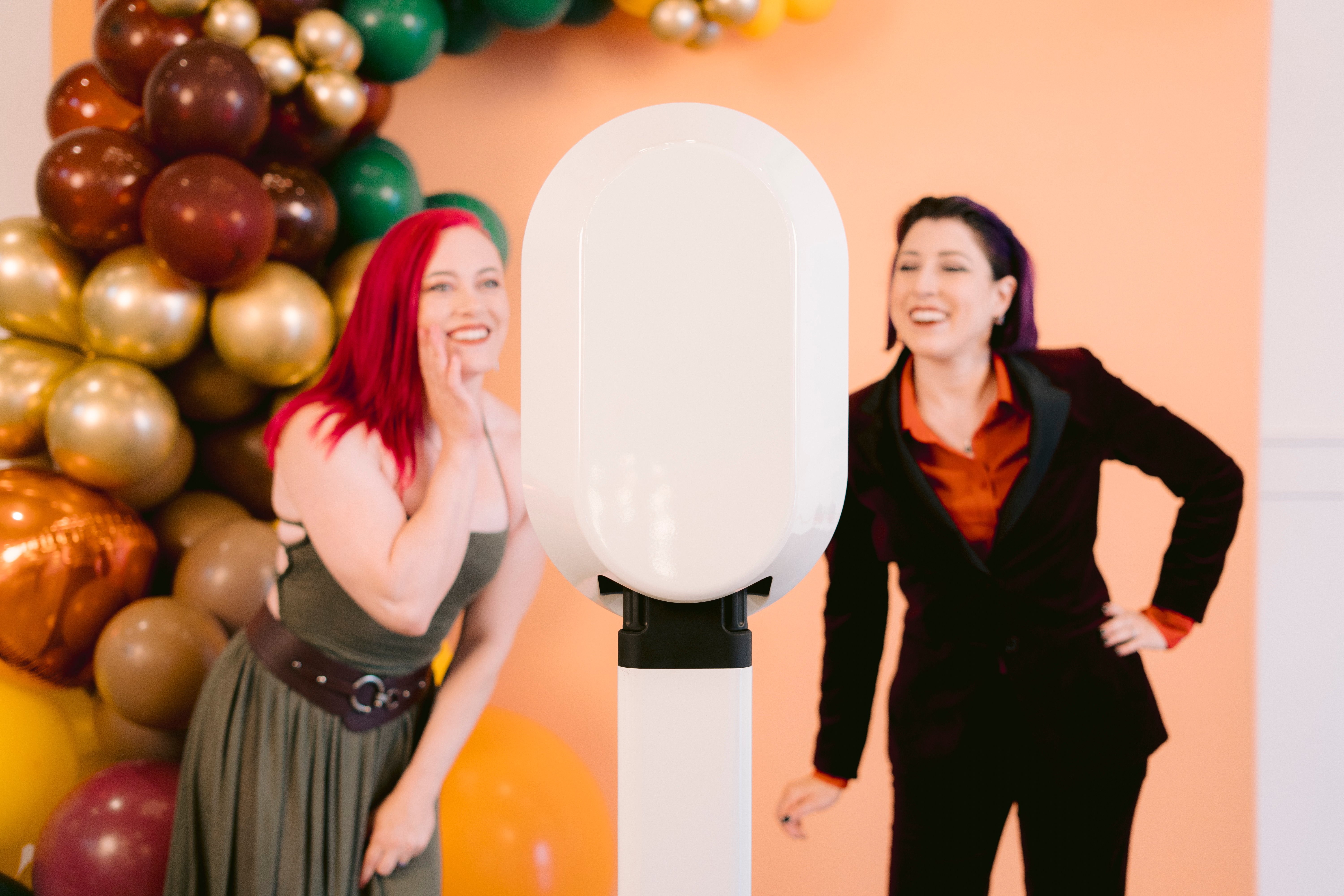 Two girls standing in front of a photo booth with an orange background and balloons